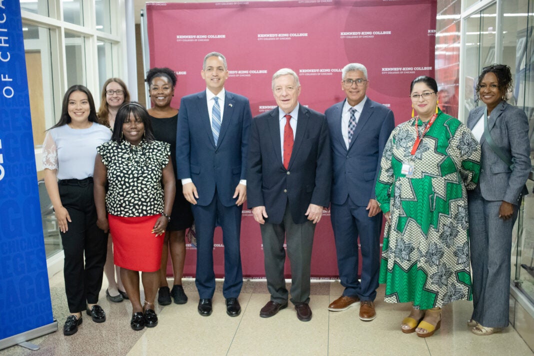 U.S. Senator Dick Durbin and City Colleges of Chicago Chancellor Juan Salgado stand in front of a red backdrop with students and college leaders on both sides of them.